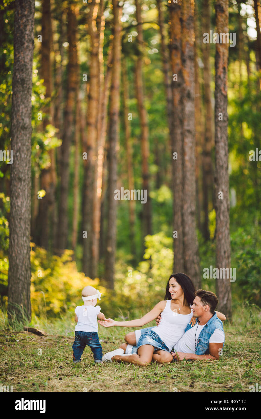 Le thème famille les loisirs de plein air dans la région de forest park. Jeune belle famille caucasienne élégant avec petit enfant fille d'un an s'asseoir sur le gr Banque D'Images