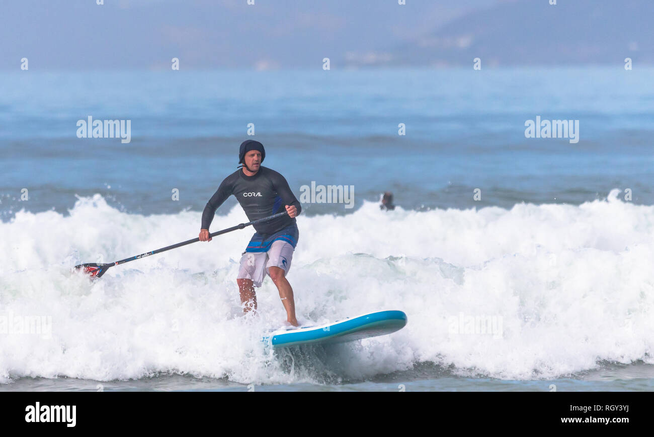 Paddleboarding sur un Stand Up Paddle ou SUP ski les vagues vers la plage sur une journée ensoleillée d'automne à Muizenberg à Cape Town, Afrique du Sud Banque D'Images