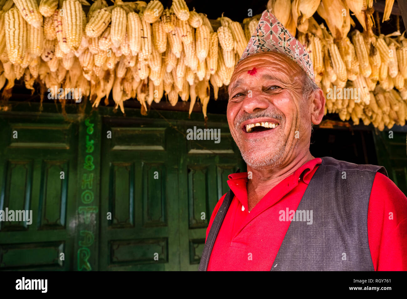 L'homme souriant, local de séchage du maïs récolté derrière lui à sa résidence. Banque D'Images