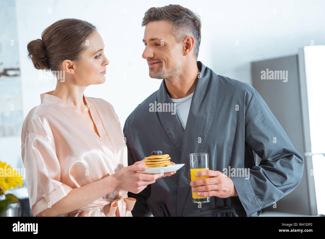 Focus sélectif de beau couple in robes avec du jus d'orange et des crêpes au petit-déjeuner dans la cuisine Banque D'Images