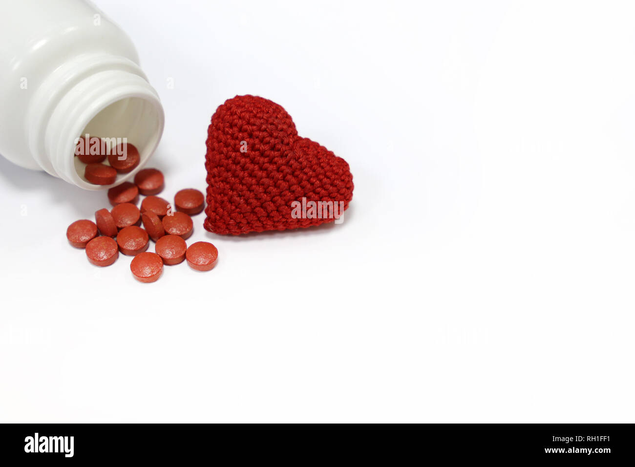 Comprimés et coeur en tricot rouge isolé sur blanc. Notion d'hypertension artérielle, les antidépresseurs, la pression artérielle, la fréquence cardiaque du traitement de la maladie Banque D'Images