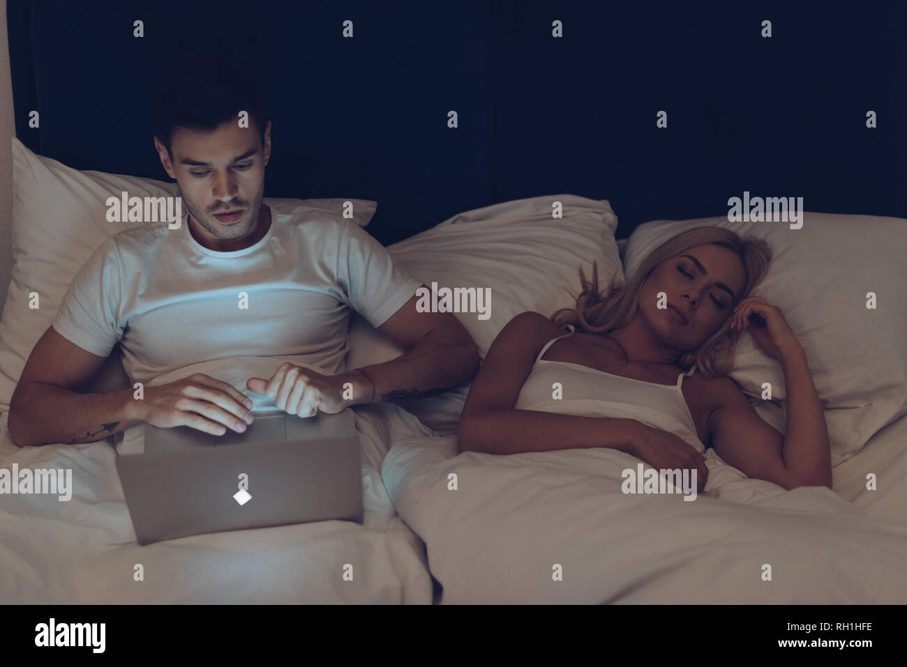 Jeune homme suspectes à l'aide d'ordinateur portable tout en belle petite amie dormant dans la nuit Banque D'Images