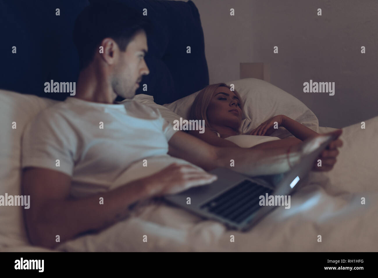 Jeune homme suspectes à l'aide d'ordinateur portable et à la copine à dormir dans la nuit Banque D'Images