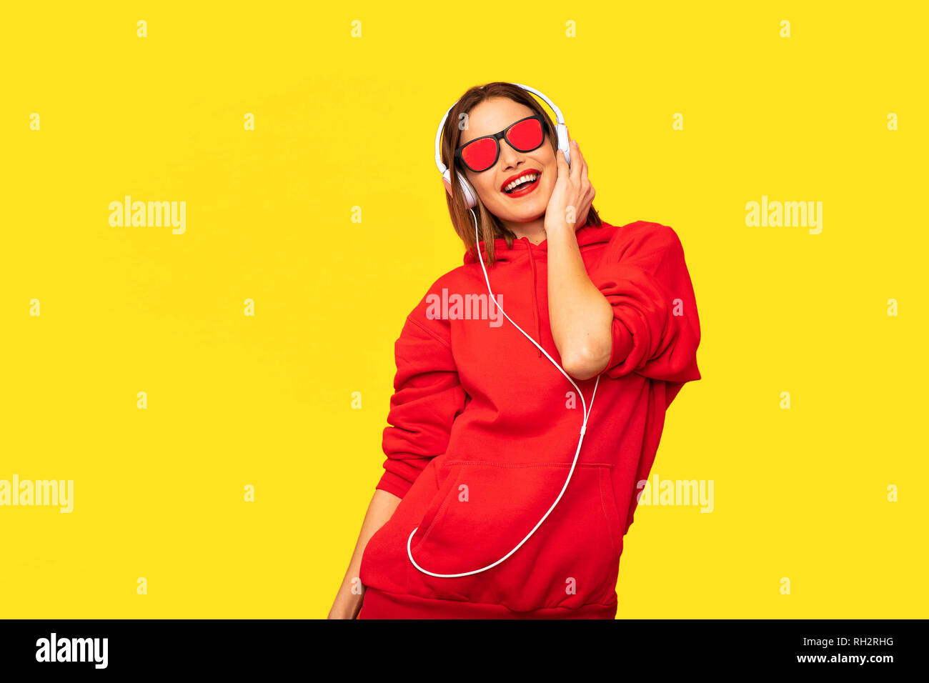 Jeune et rebel Girl in red hoodie avec casques et lunettes à l'écoute de la musique, cool hipster Banque D'Images