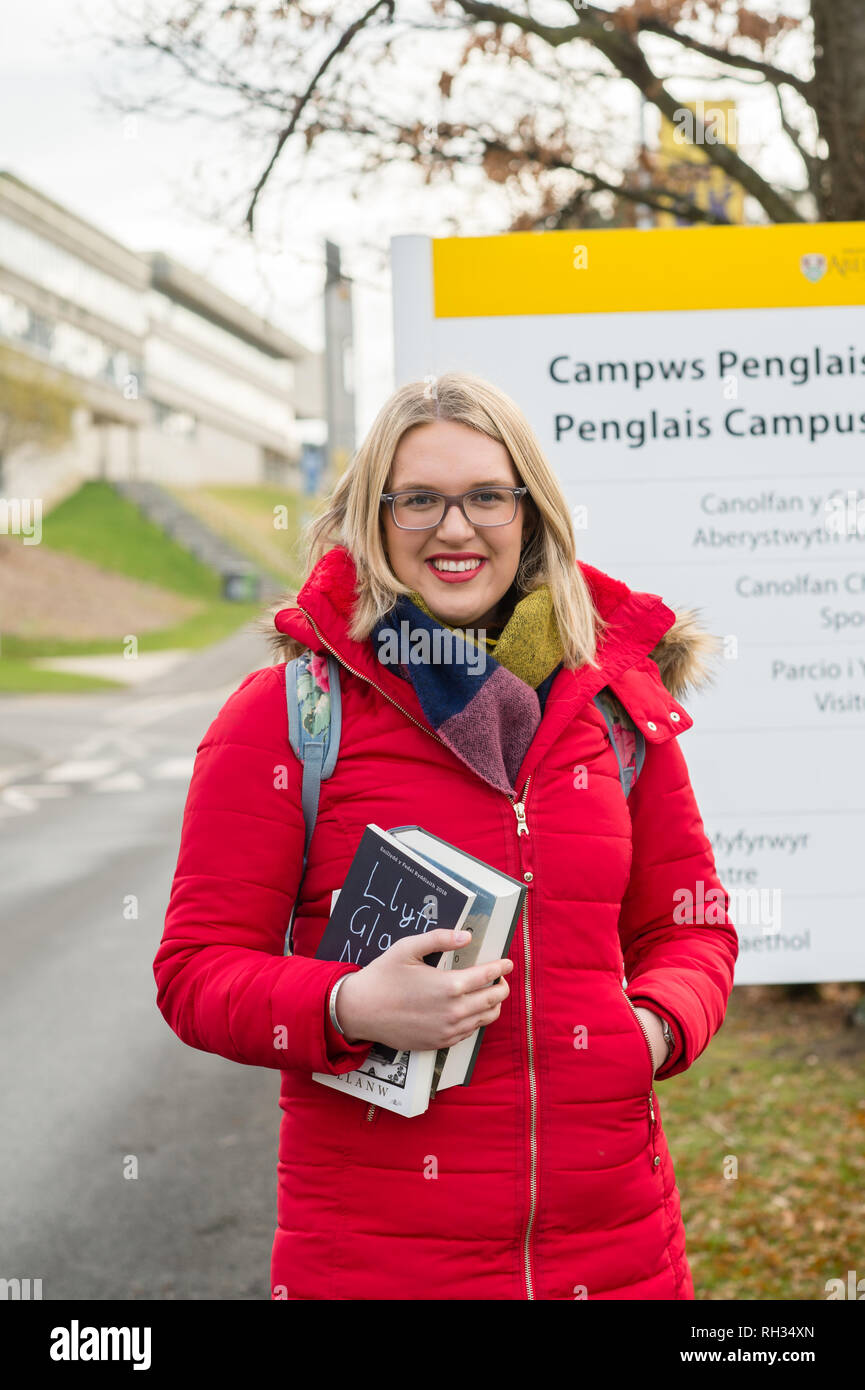 Une première année de premier cycle étudiante , à l'Université d'Aberystwyth, Pays de Galles, UK - portant un manteau rouge et tenant son texte livres sur le campus du collège Banque D'Images