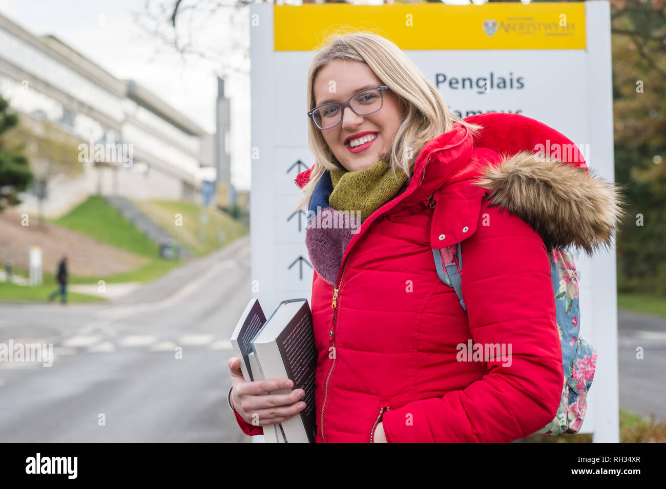 Une première année de premier cycle étudiante , à l'Université d'Aberystwyth, Pays de Galles, UK - portant un manteau rouge et tenant son texte livres sur le campus du collège Banque D'Images