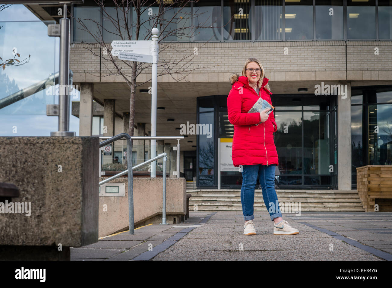 Une première année de premier cycle étudiante , à l'Université d'Aberystwyth, Pays de Galles, UK - portant un manteau rouge et tenant son texte livres sur le campus du collège Banque D'Images