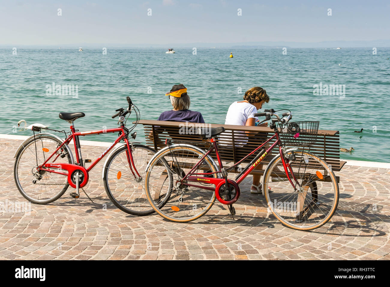 Torri del Benaco, Lac de Garde, ITALIE - Septembre 2018 : deux vélos laissé contre un siège sur la promenade de Lazise sur le lac de garde pendant que leurs cavaliers prennent une pause Banque D'Images