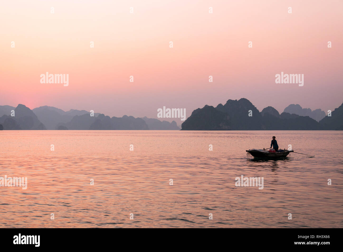 Une Vietnamienne aviron bateau en bois avec ses îles karstiques de calcaire en arrière-plan au coucher du soleil, la baie d'Halong, Vietnam Banque D'Images