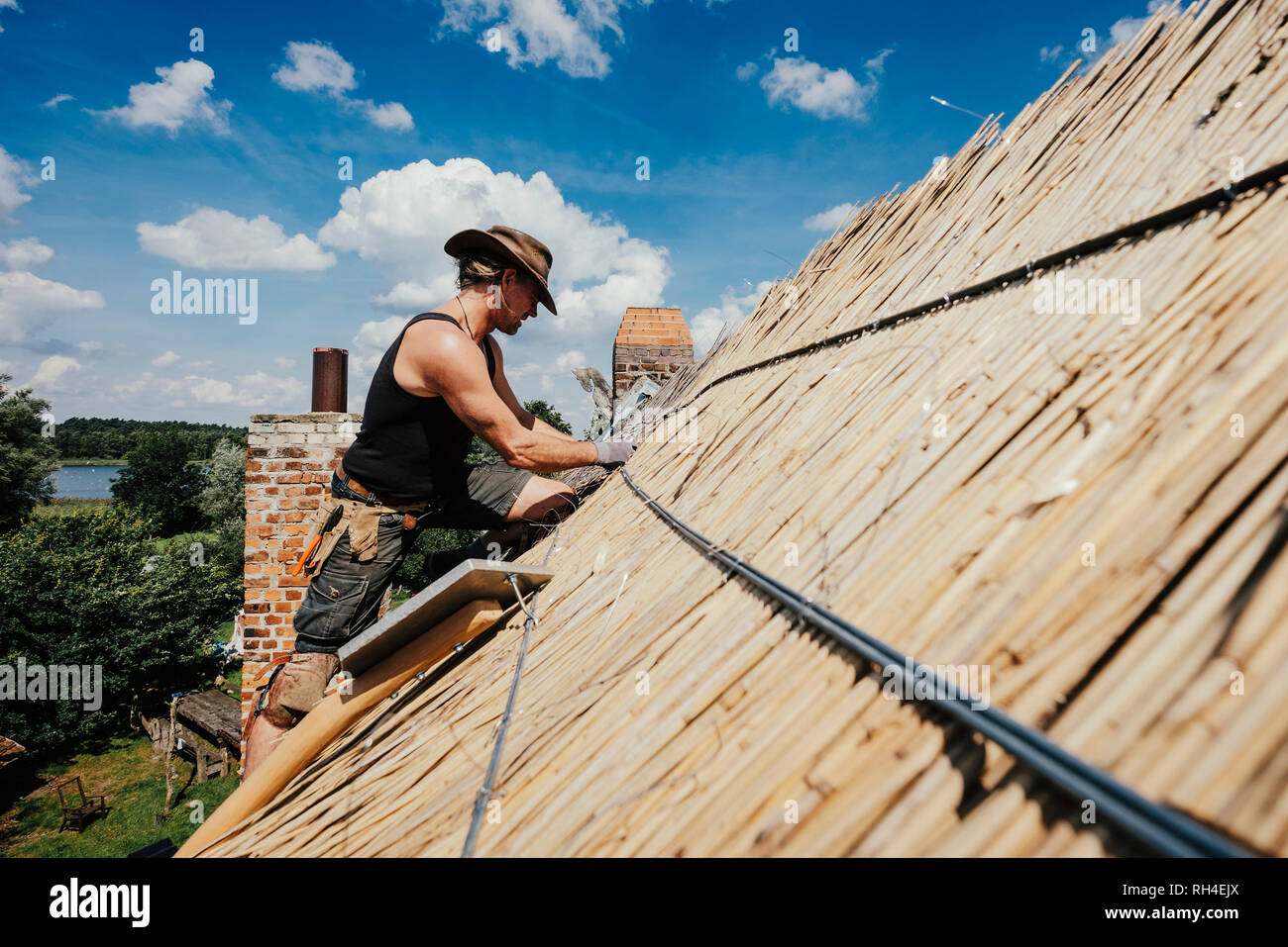L'homme de réparer un toit de chaume sur sunny house Banque D'Images