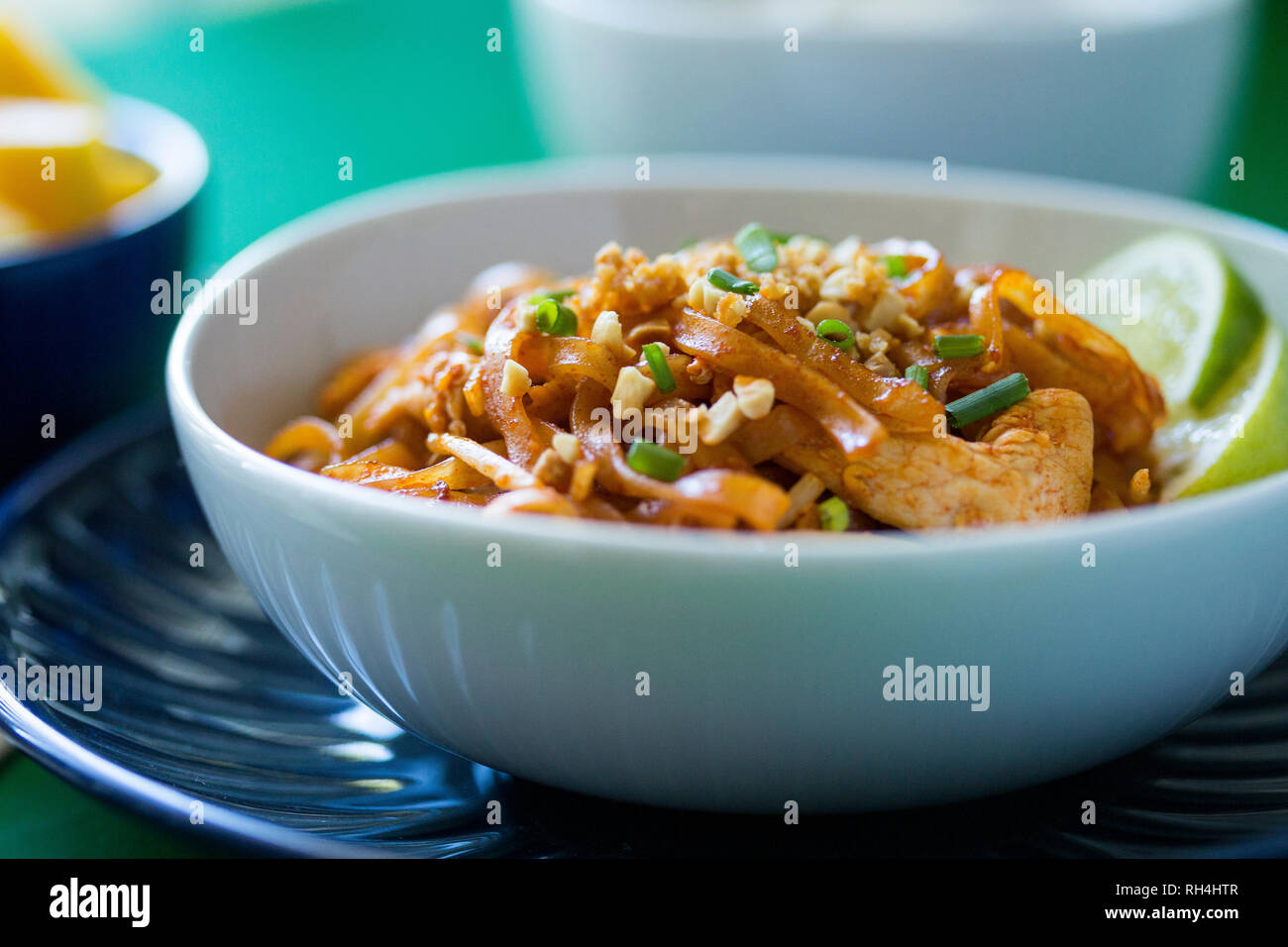 Bol de nouilles Pad Thaï au poulet, l'arachide, l'oignon vert, et de la chaux sur les plaques bleu et blanc et coloré de la surface verte. Banque D'Images