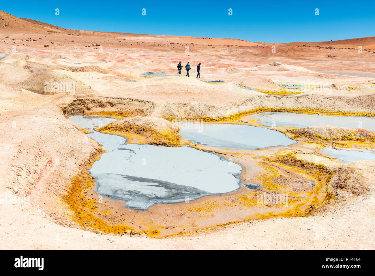 Trois touristes marcher par la boue des fosses, des fumerolles et des geysers de Sol de Manana près de la télévision sel Uyuni (Salar de Uyuni) dans l'Altiplano de Bolivie. Banque D'Images