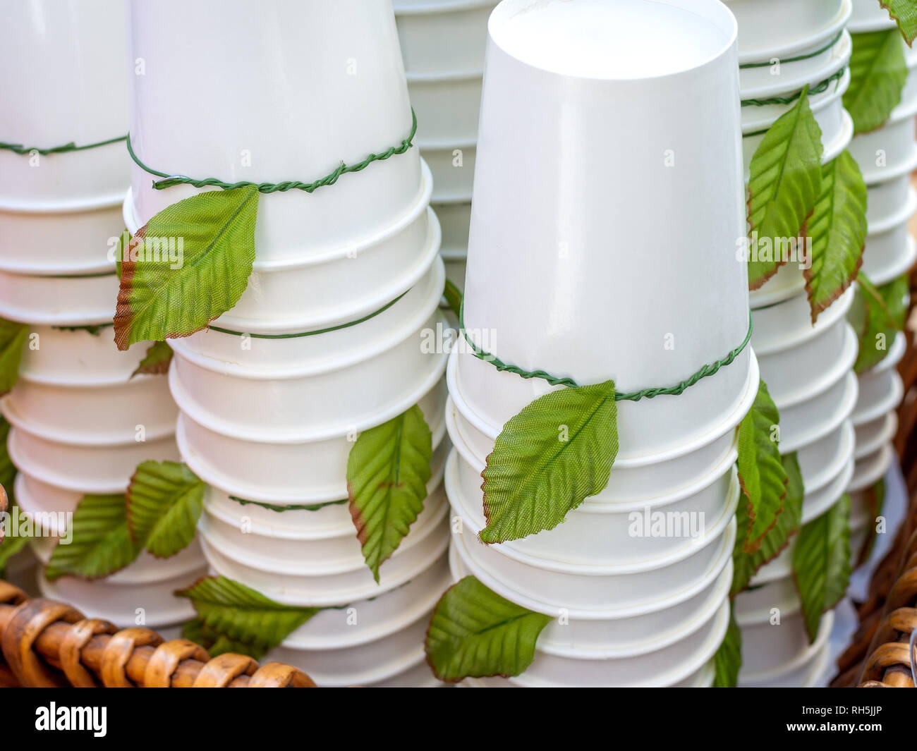 Tasses jetables blanc à l'envers. Des piles de papier blanc décoration tasses avec des feuilles vertes dans le panier. Banque D'Images