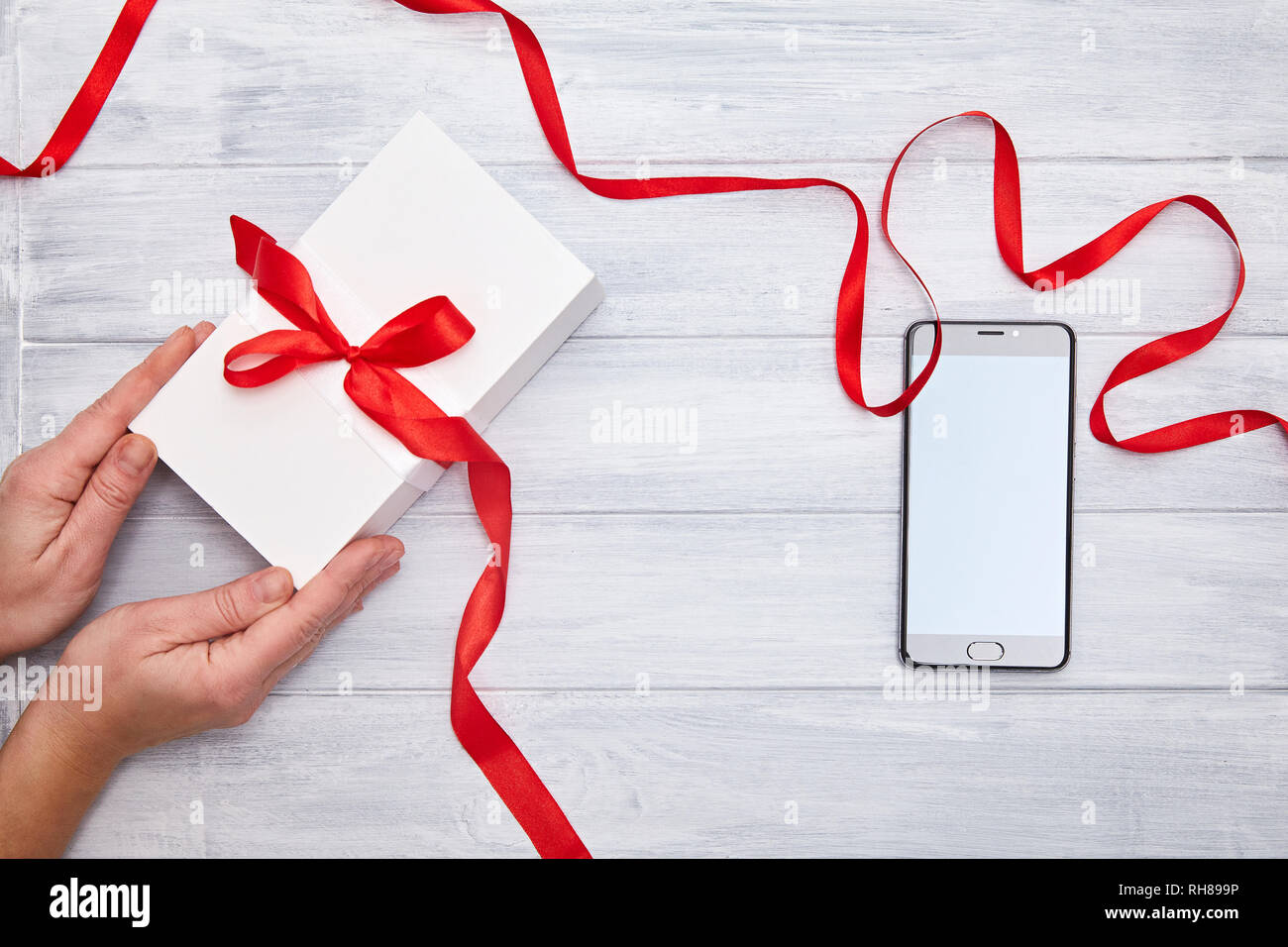 Boîte cadeau blanche dans les mains avec du ruban rouge et le smartphone  sur un fond woodem. Anniversaire, Noël, la Saint Valentin cadeau concept  Photo Stock - Alamy