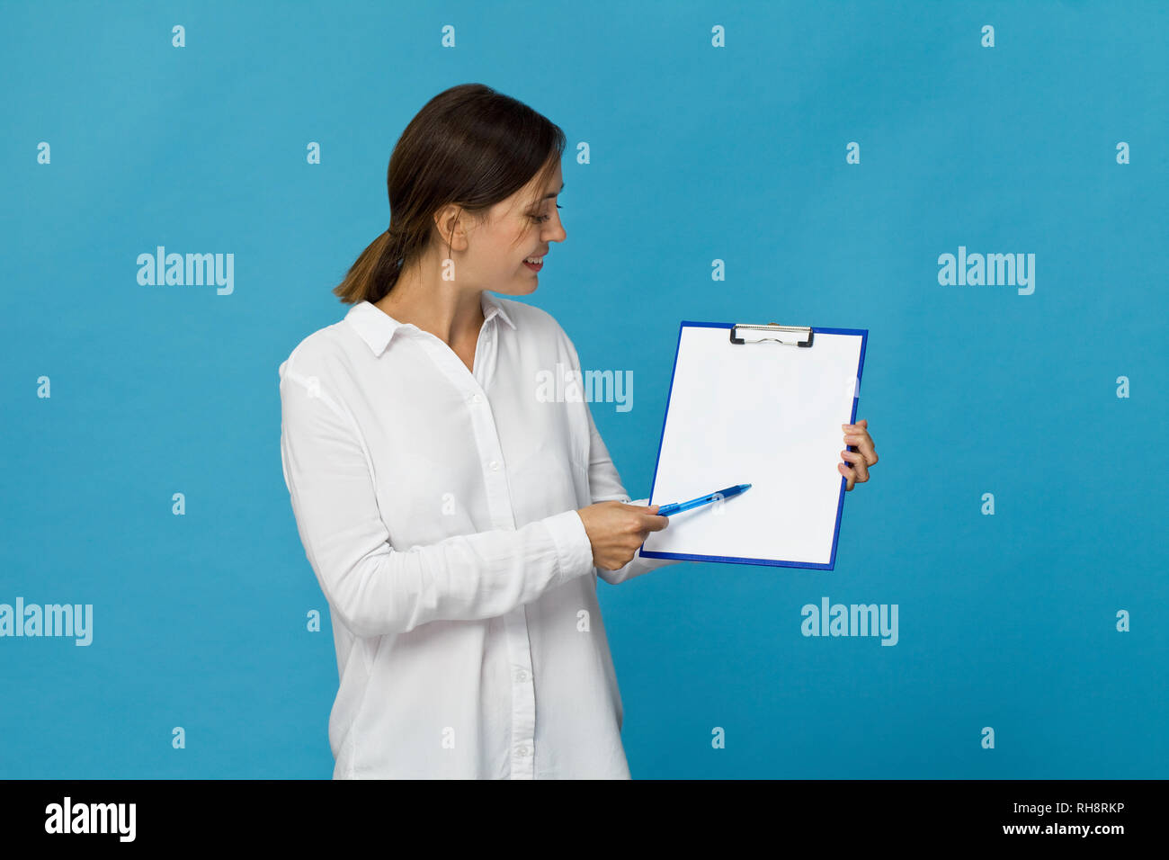 Happy brunette woman in white shirt élégant showing blank presse-papiers, isolated on white Banque D'Images