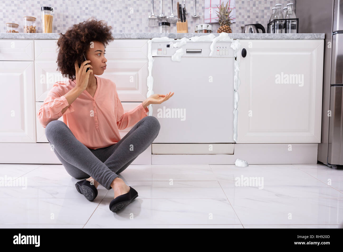 Triste femme appelant Technicien sur téléphone cellulaire pour réparer lave- vaisselle avec de la mousse qui sort de c Photo Stock - Alamy