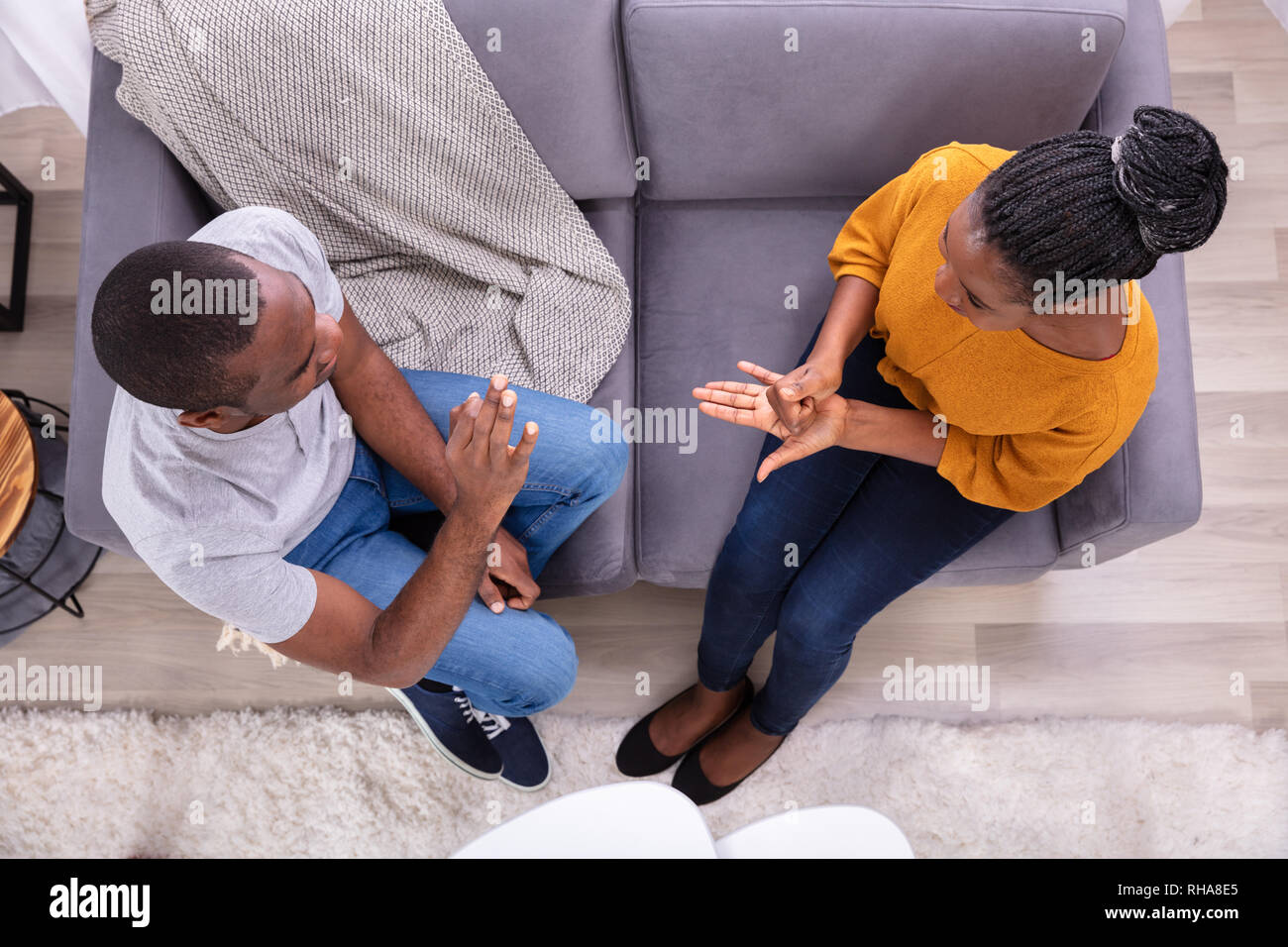Smiling Young Couple Sitting on Sofa Communication avec les langues des signes Banque D'Images