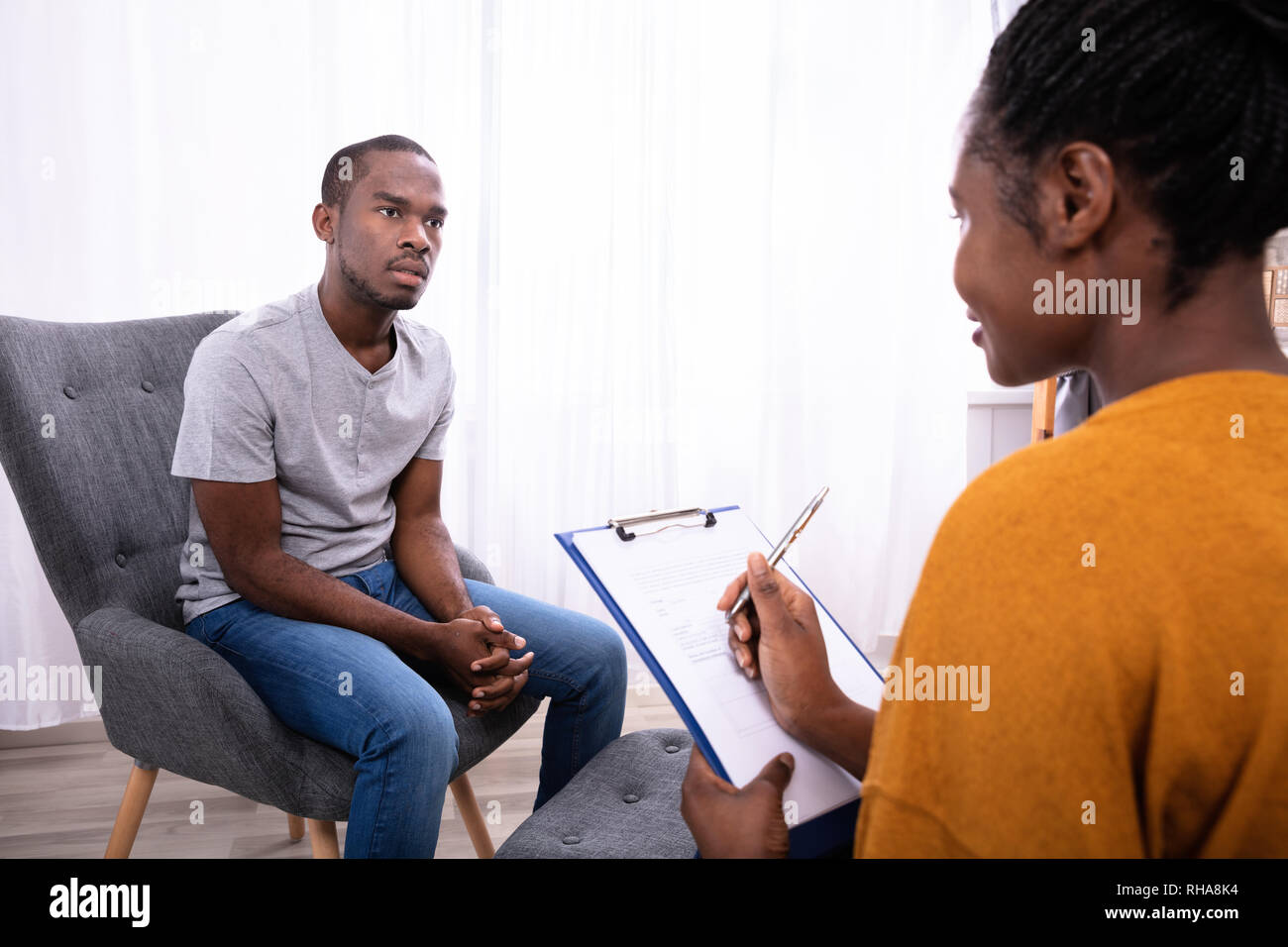 Jeune homme africain assis sur une chaise près de psychologue femelle avec  presse-papiers Photo Stock - Alamy