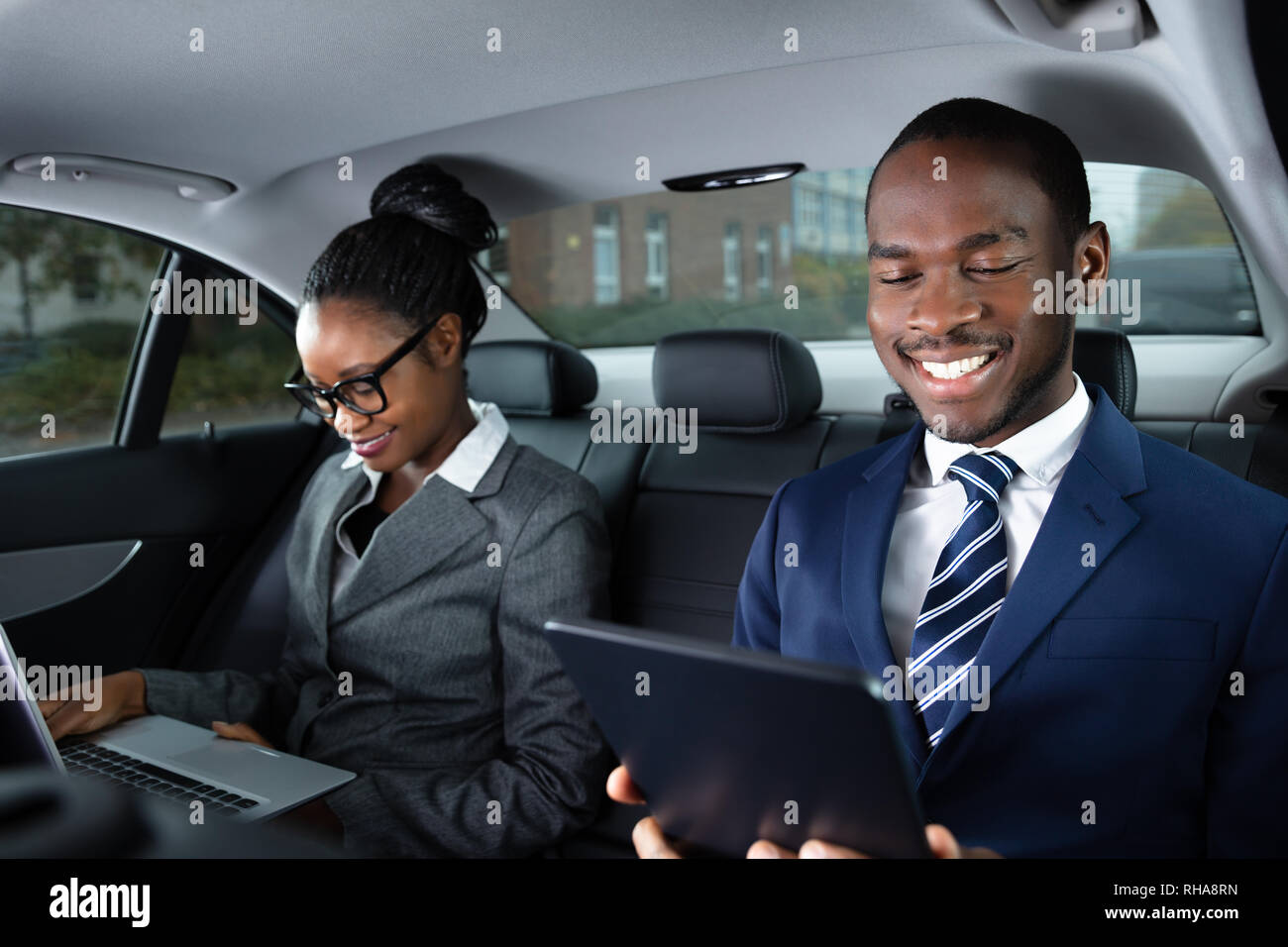 Deux heureux d'affaires africaines à l'aide d'appareils électroniques tout en voyageant en voiture Banque D'Images