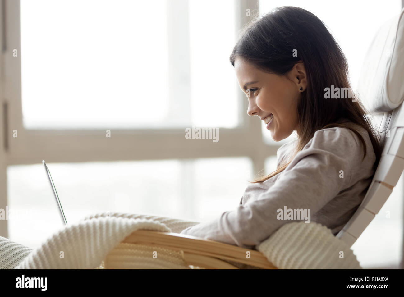 Happy smiling young woman using laptop sitting on rocking chair Banque D'Images