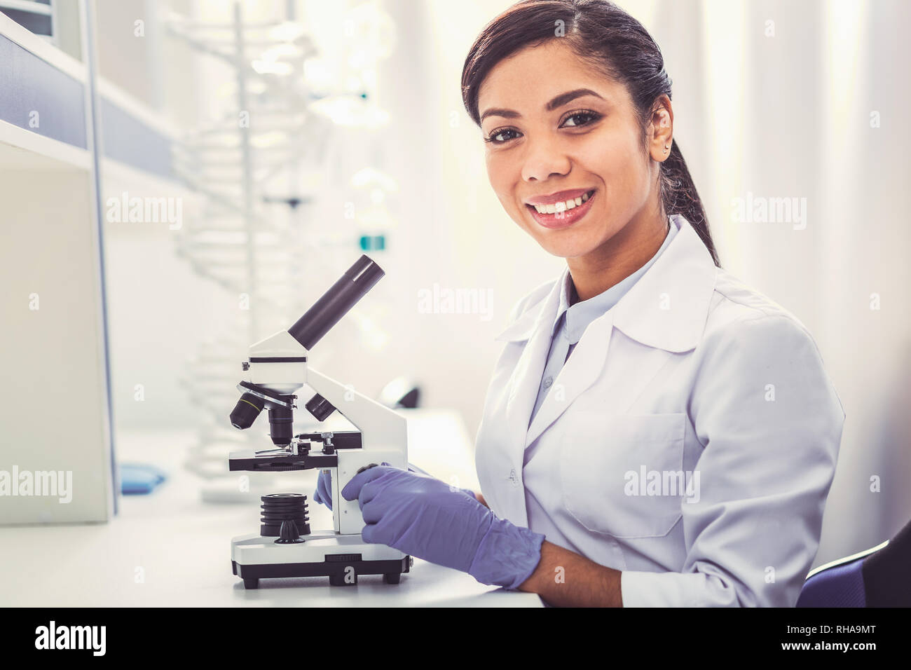 Jeune chimiste portant des uniformes blancs assis près de microscope Banque D'Images
