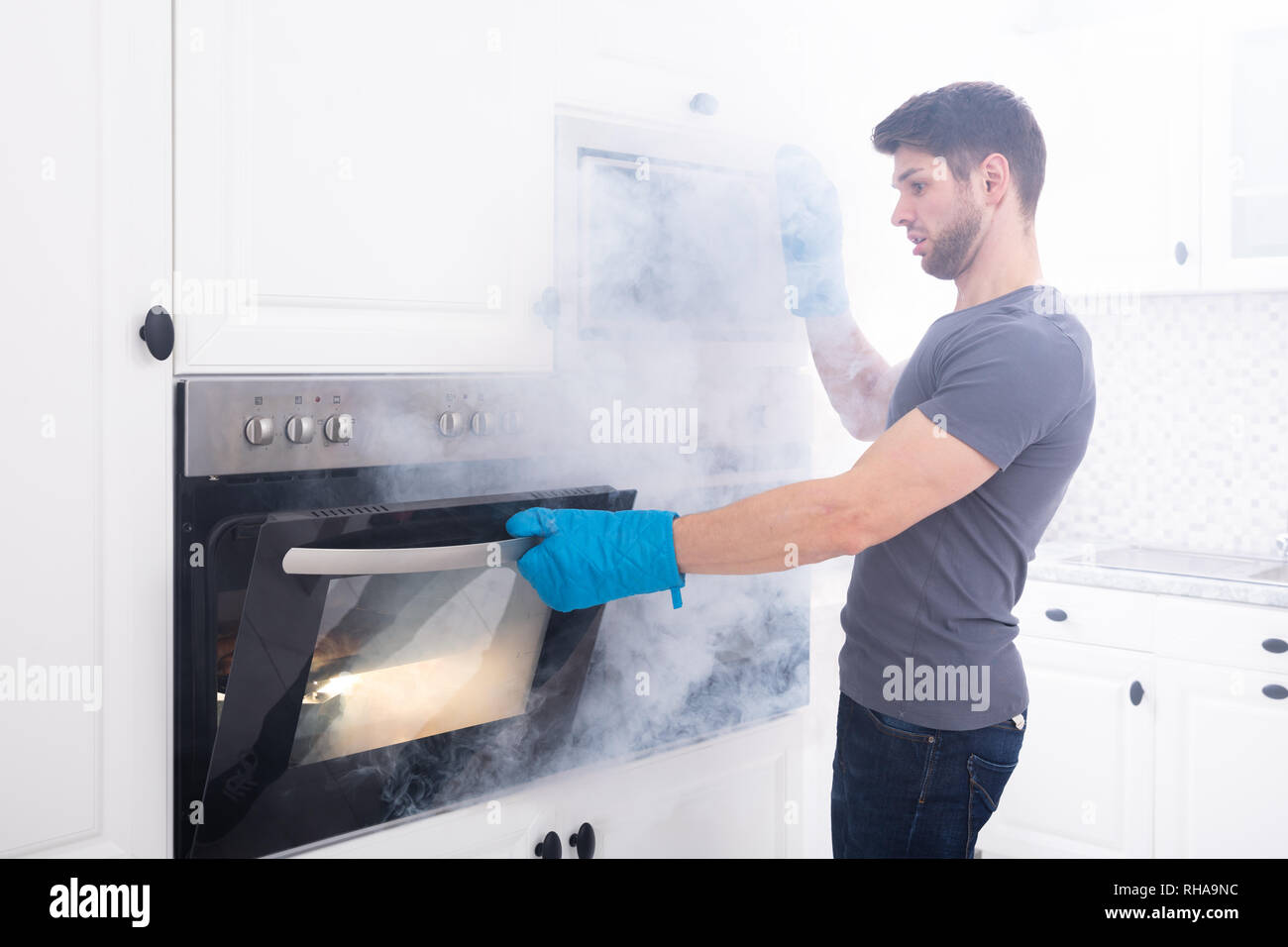 Jeune homme portant des gants Four Ouverture remplie de fumée dans la cuisine Banque D'Images