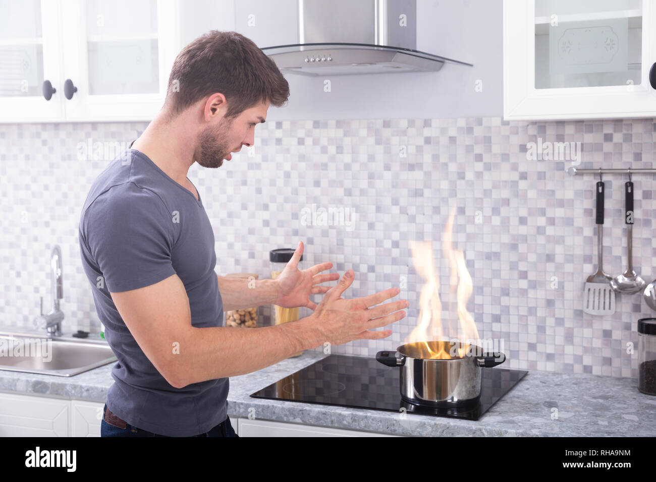 Jeune homme choqué à la marmite à brûler avec le feu sur l'induction Cuisinière Banque D'Images