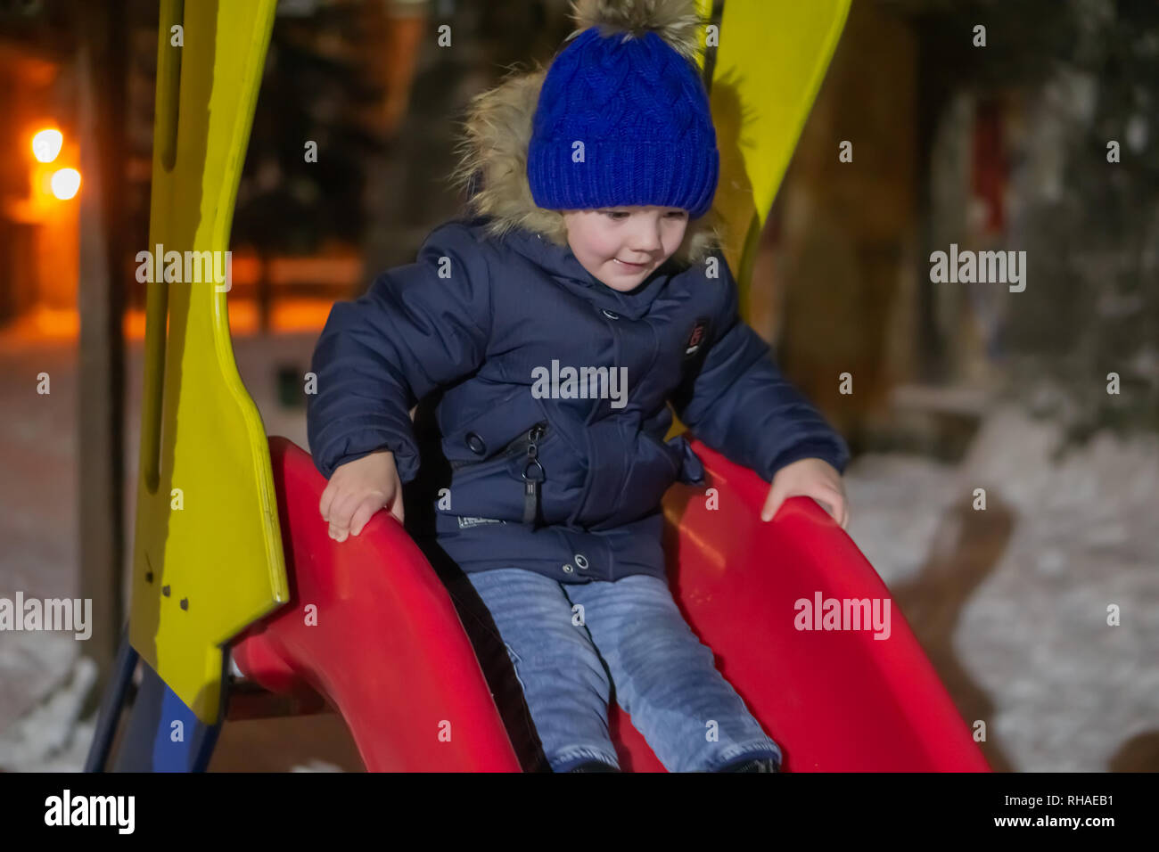 Un garçon de trois ans qui dans la vie de tous les jours des vêtements d'hiver est de descendre une colline. Il est heureux et aime jouer dans le froid. Banque D'Images