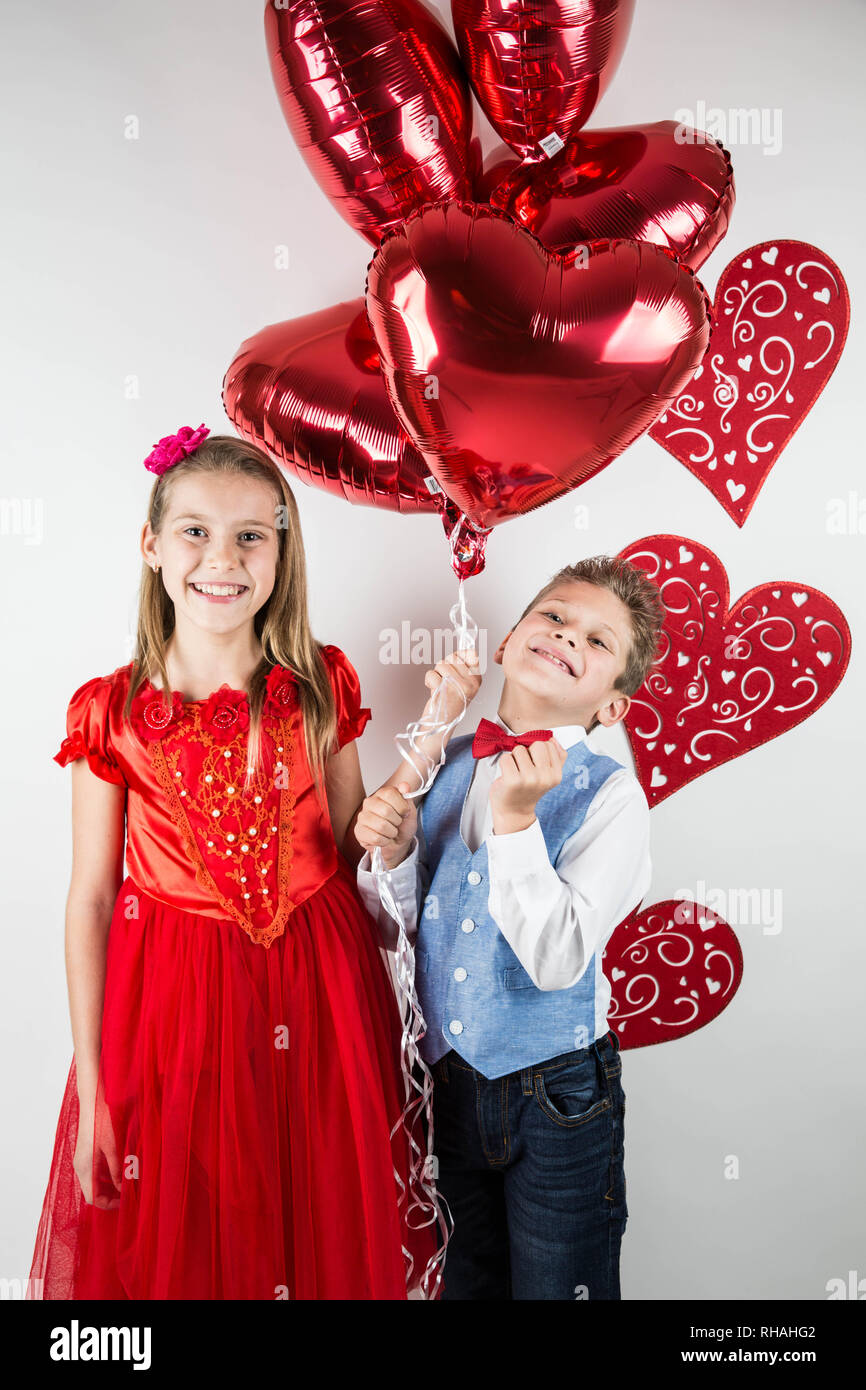 Saint Valentine's day. Jolie fille avec robe rouge et gentleman garçon avec gilet bleu, rouge cravate papillon, roses rouges en forme de coeur et godet boîte-cadeau. Va Banque D'Images