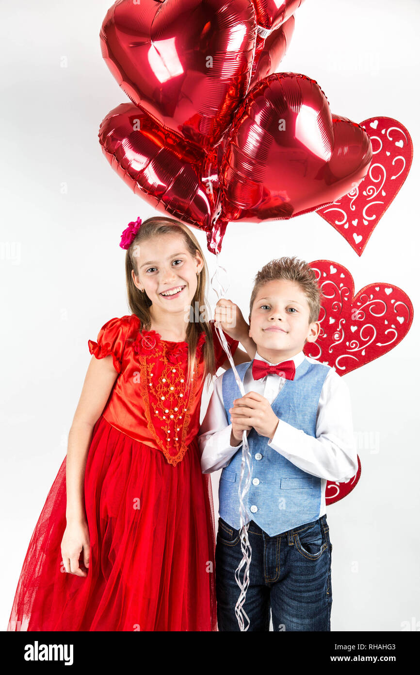 Saint Valentine's day. Jolie fille avec robe rouge et gentleman garçon avec gilet bleu, rouge cravate papillon, roses rouges en forme de coeur et godet boîte-cadeau. Va Banque D'Images