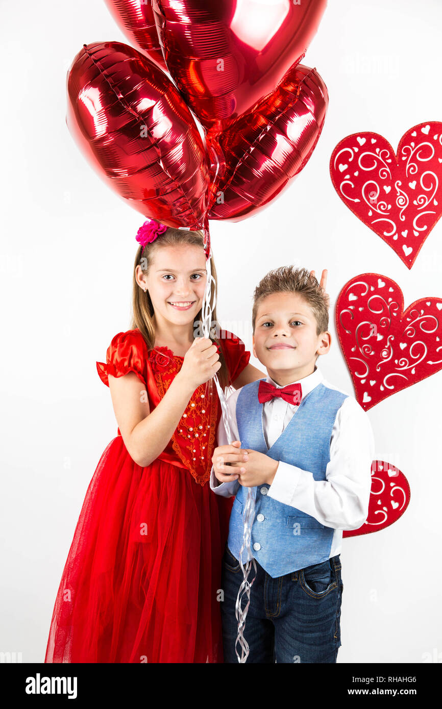 Saint Valentine's day. Jolie fille avec robe rouge et gentleman garçon avec gilet bleu, rouge cravate papillon, roses rouges en forme de coeur et godet boîte-cadeau. Va Banque D'Images