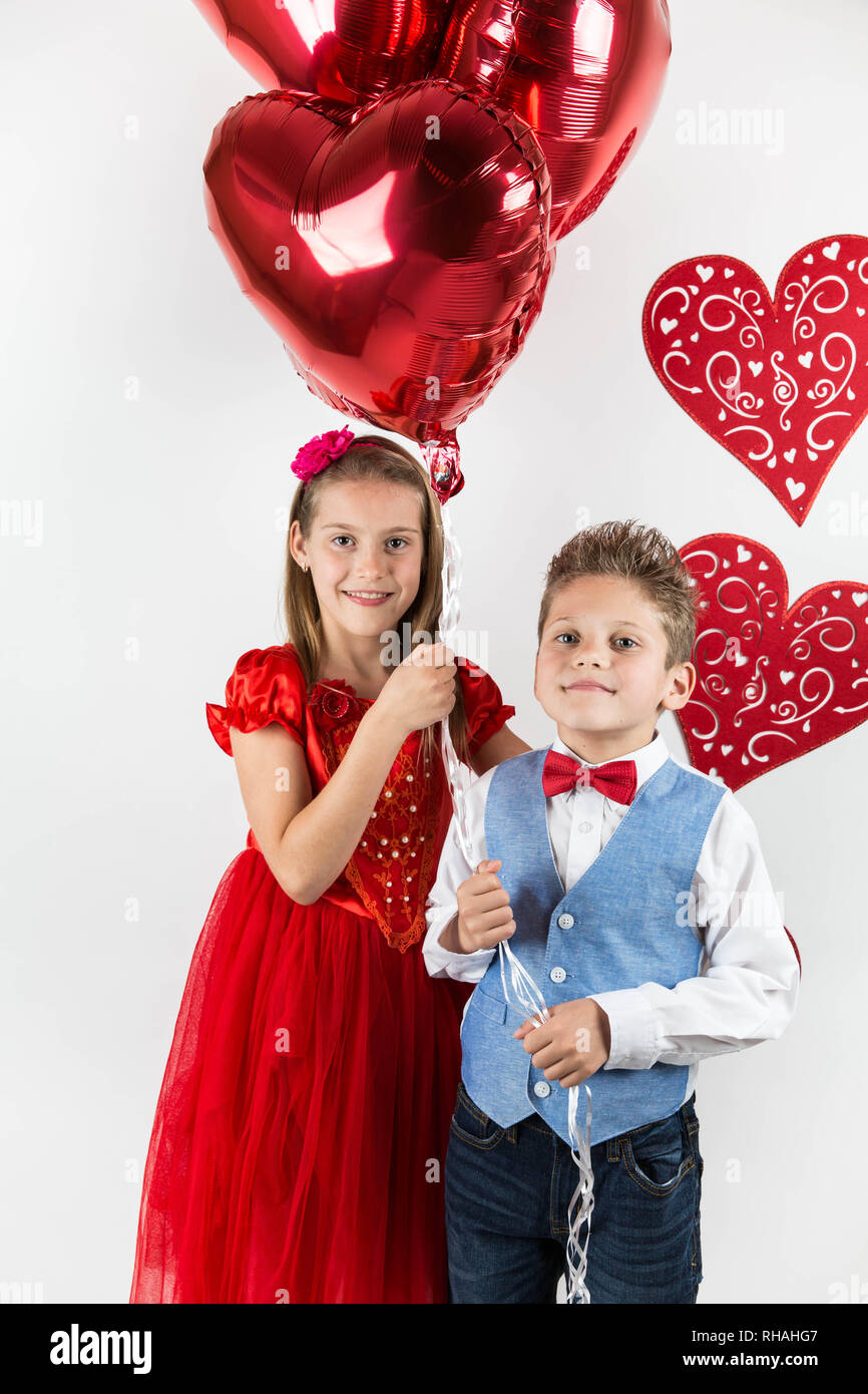 Saint Valentine's day. Jolie fille avec robe rouge et gentleman garçon avec gilet bleu, rouge cravate papillon, roses rouges en forme de coeur et godet boîte-cadeau. Va Banque D'Images