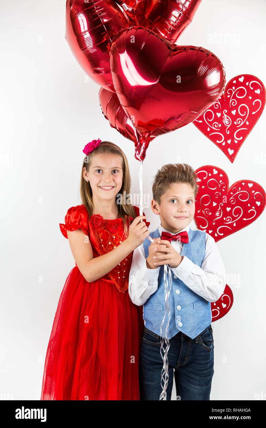 Saint Valentine's day. Jolie fille avec robe rouge et gentleman garçon avec gilet bleu, rouge cravate papillon, roses rouges en forme de coeur et godet boîte-cadeau. Va Banque D'Images