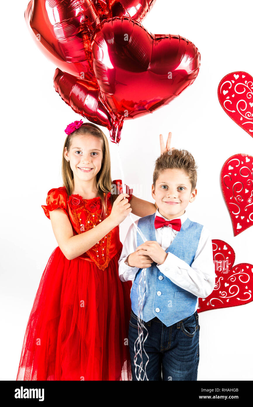 Saint Valentine's day. Jolie fille avec robe rouge et gentleman garçon avec gilet bleu, rouge cravate papillon, roses rouges en forme de coeur et godet boîte-cadeau. Va Banque D'Images