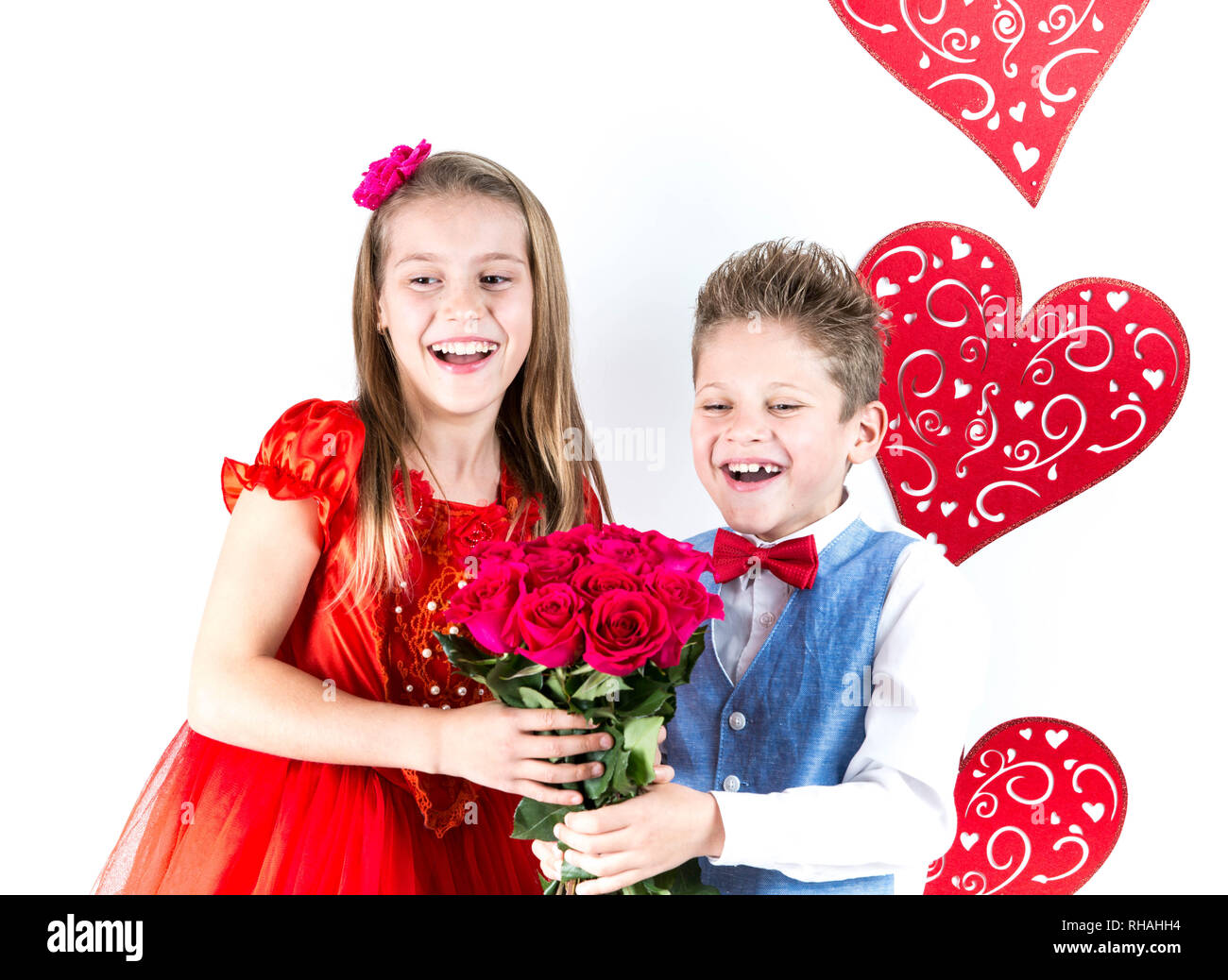 Saint Valentine's day. Jolie fille avec robe rouge et gentleman garçon avec gilet bleu, rouge cravate papillon, roses rouges en forme de coeur et godet boîte-cadeau. Va Banque D'Images