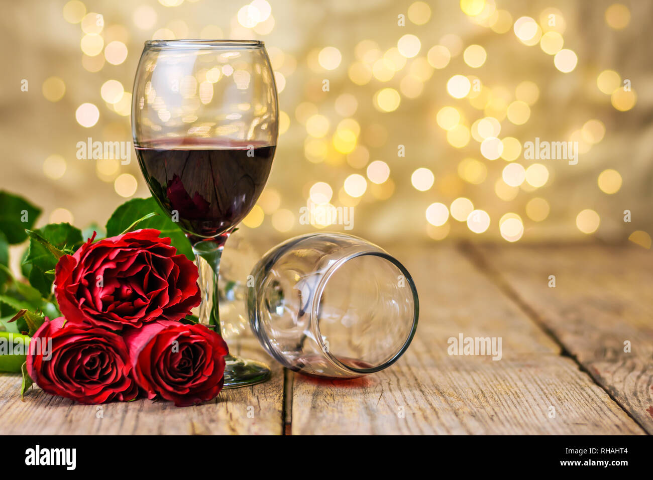 Valentine's Day still life. Deux verres de vin et de roses rouges sur une table rustique en bois en face d'un flou d'arrière-plan lumineux. Focus sélectif. Banque D'Images