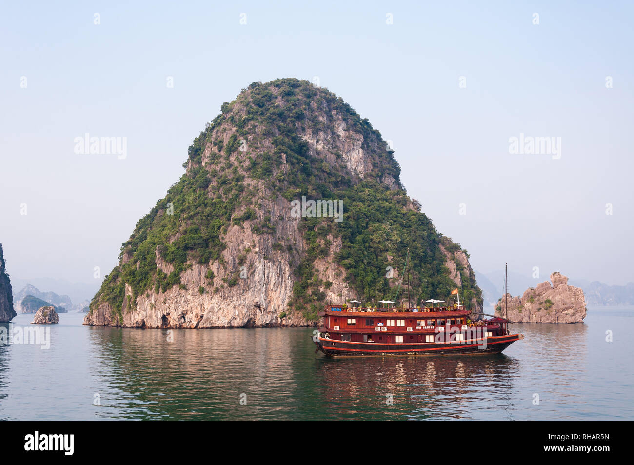 Une jonque touristique en bois ancrée par un karst calcaire island in early morning light, Halong Bay, Vietnam Banque D'Images