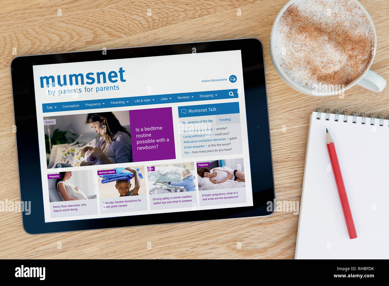 Le site web dispose d'un Mumsnet iPad tablet device qui repose sur une table en bois à côté d'un bloc-notes (usage éditorial uniquement). Banque D'Images
