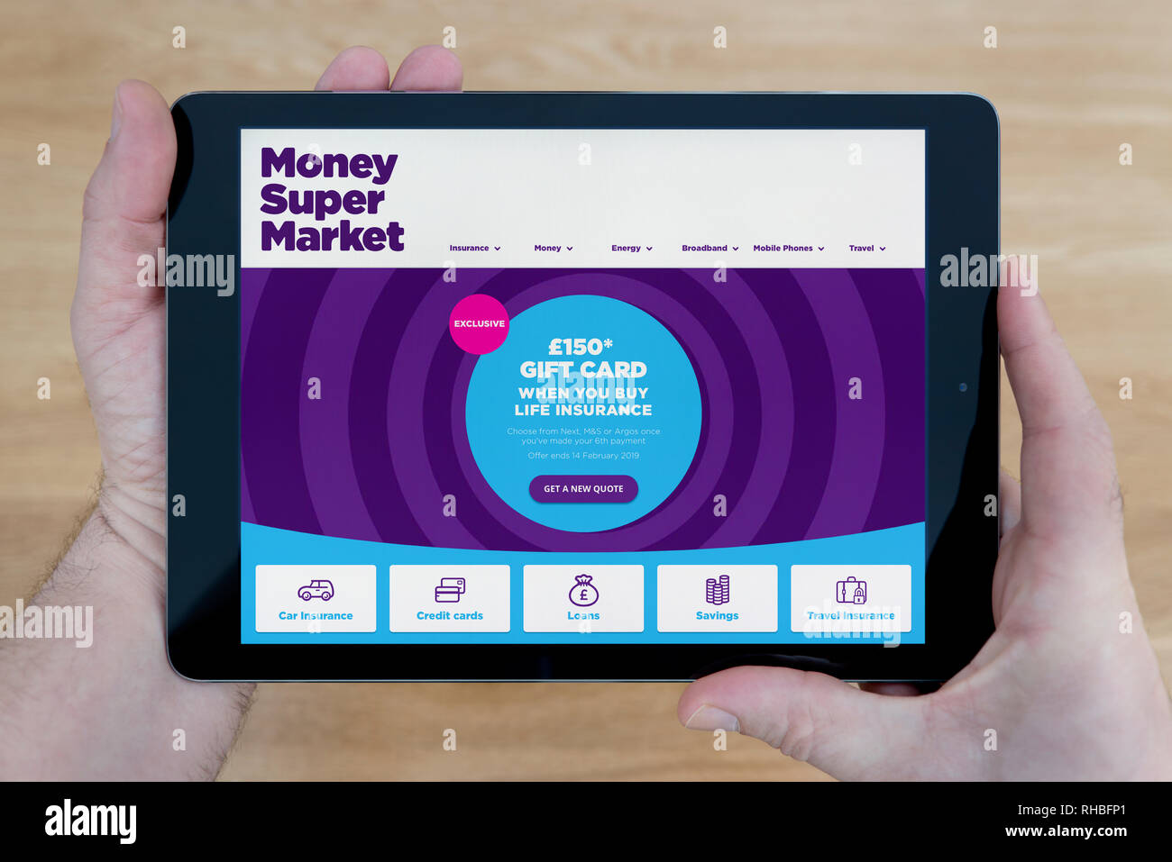 Un homme regarde le site web de MoneySuperMarket sur son iPad tablet device, tourné contre une table en bois page contexte (usage éditorial uniquement). Banque D'Images