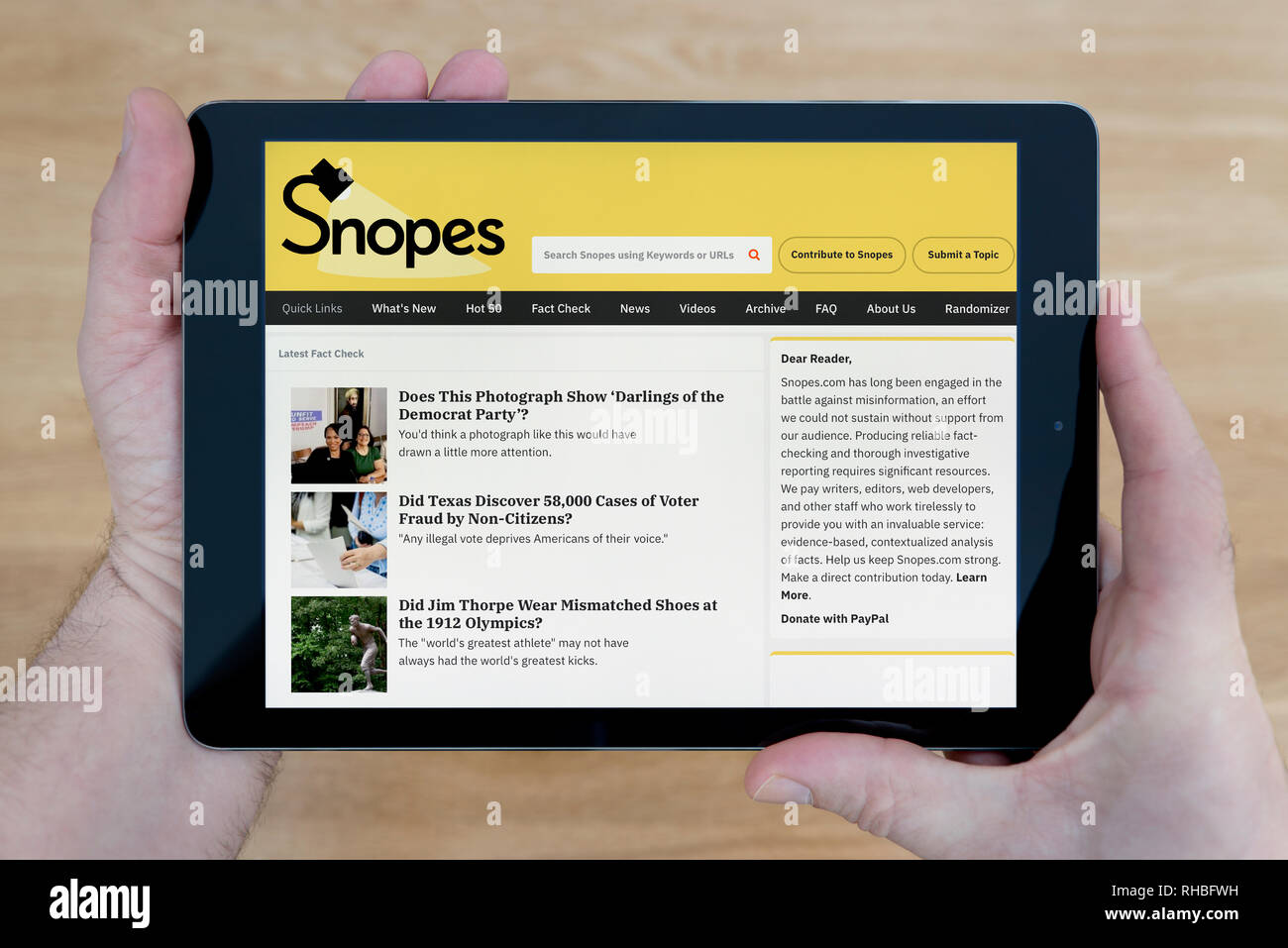 Un homme regarde le site Snopes sur son iPad tablet device, tourné contre une table en bois page contexte (usage éditorial uniquement). Banque D'Images