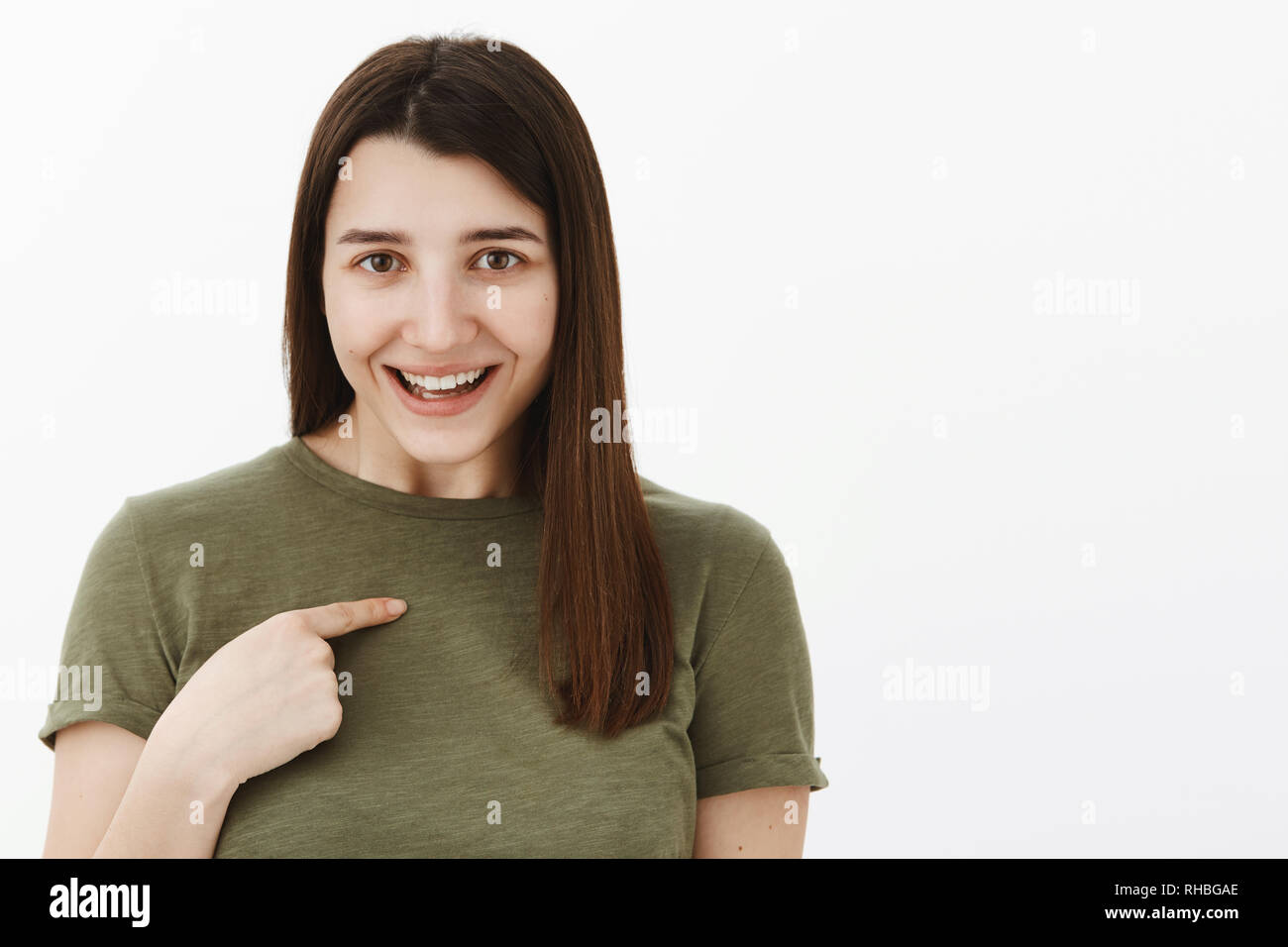 Vous parler de moi. Portrait de surpris et heureux charming brunette en 20s portant des T-shirt olive heureusement souriant comme pointant sur sa poitrine Banque D'Images