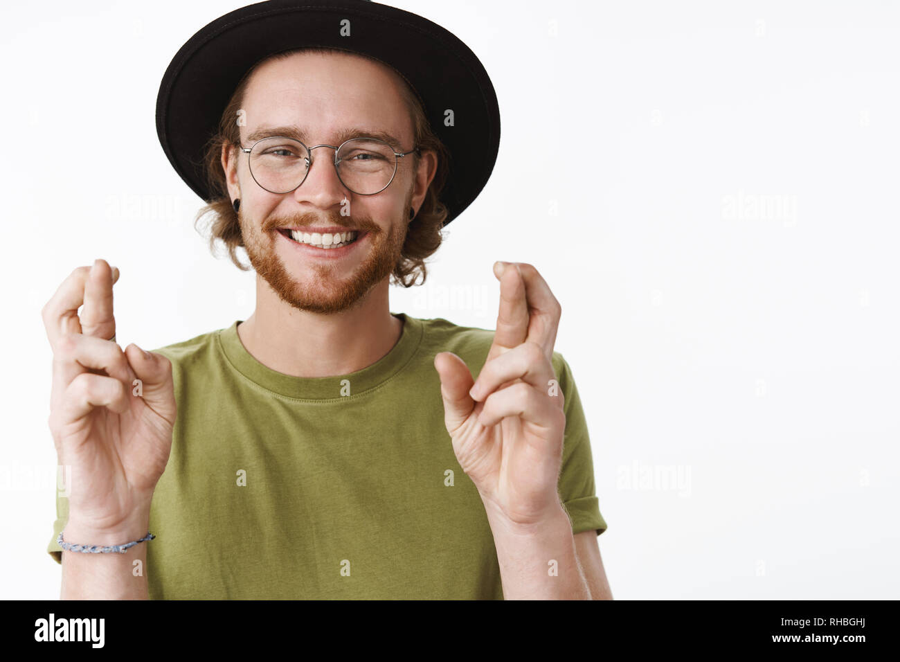 Jusqu'à la taille de balle heureux et sincère genre jeune homme barbu traveler décisions espère ou avec les mains et les doigts croisés, souriant à optimiste Banque D'Images