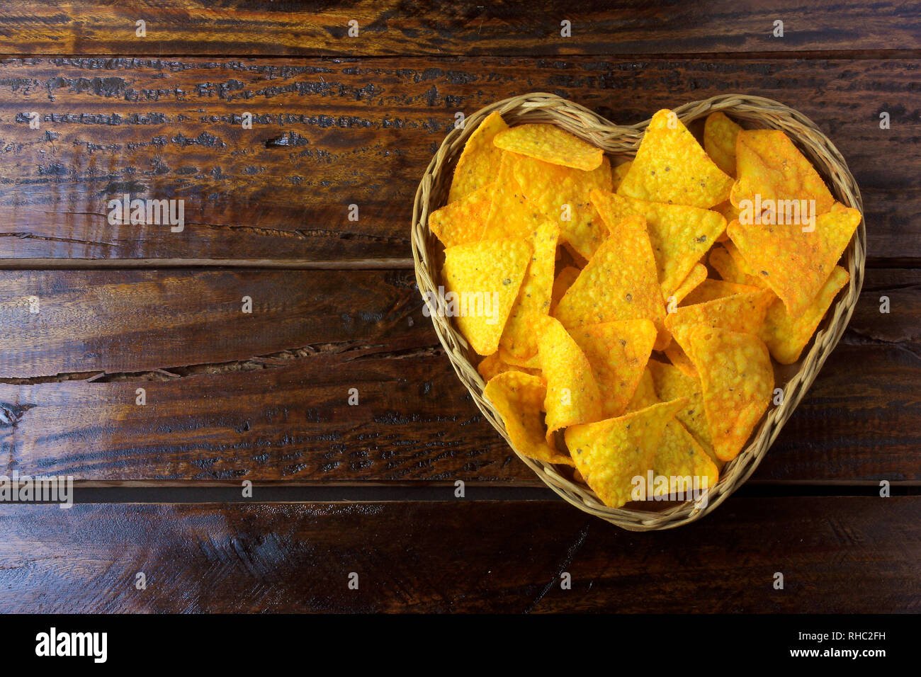 Nachos croustilles de maïs placés dans panier avec forme de coeur sur table en bois, de l'espace pour le texte Banque D'Images