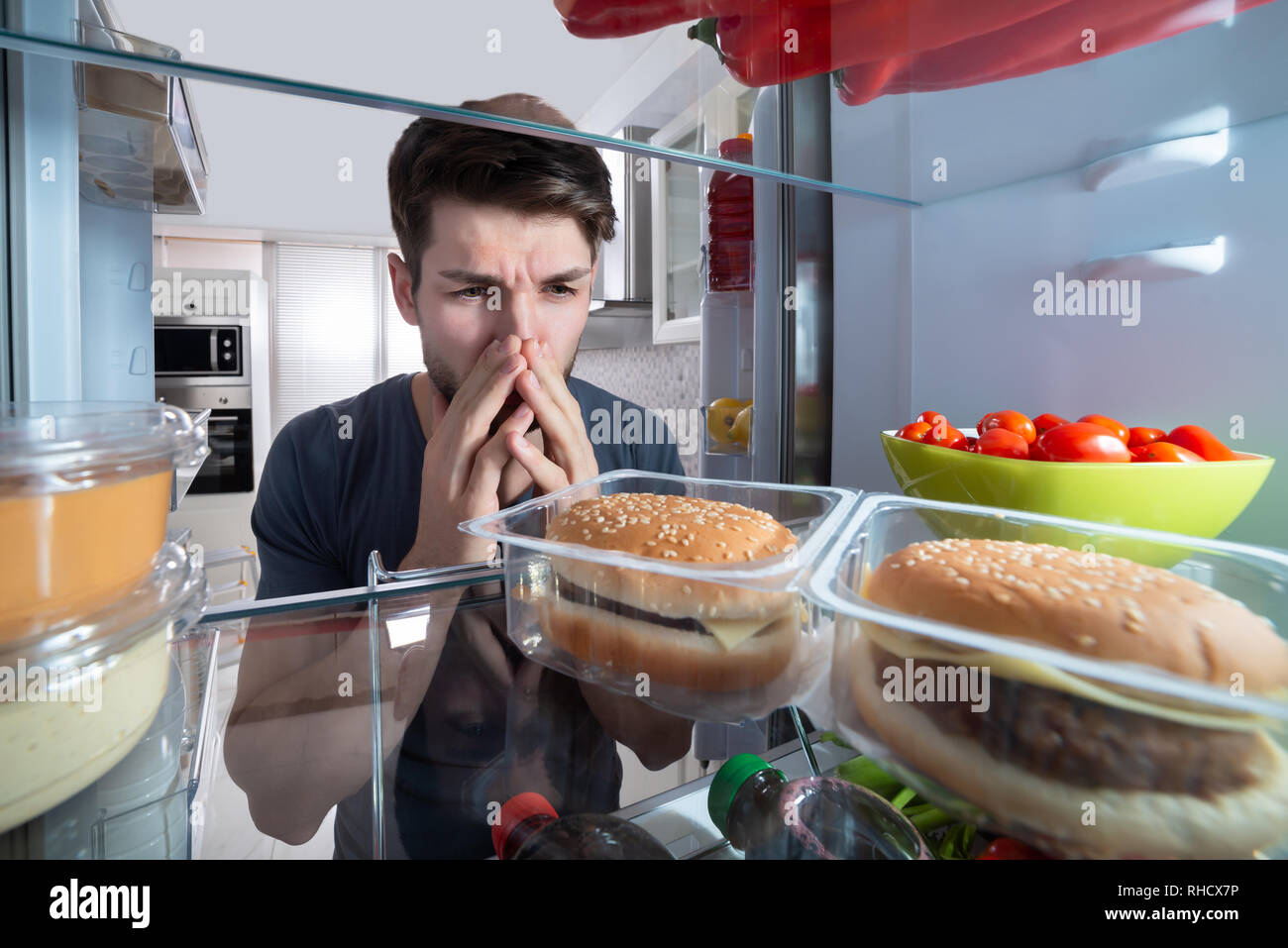 Jeune homme tenant son nez après avoir reconnu la mauvaise odeur qui sort du réfrigérateur Banque D'Images
