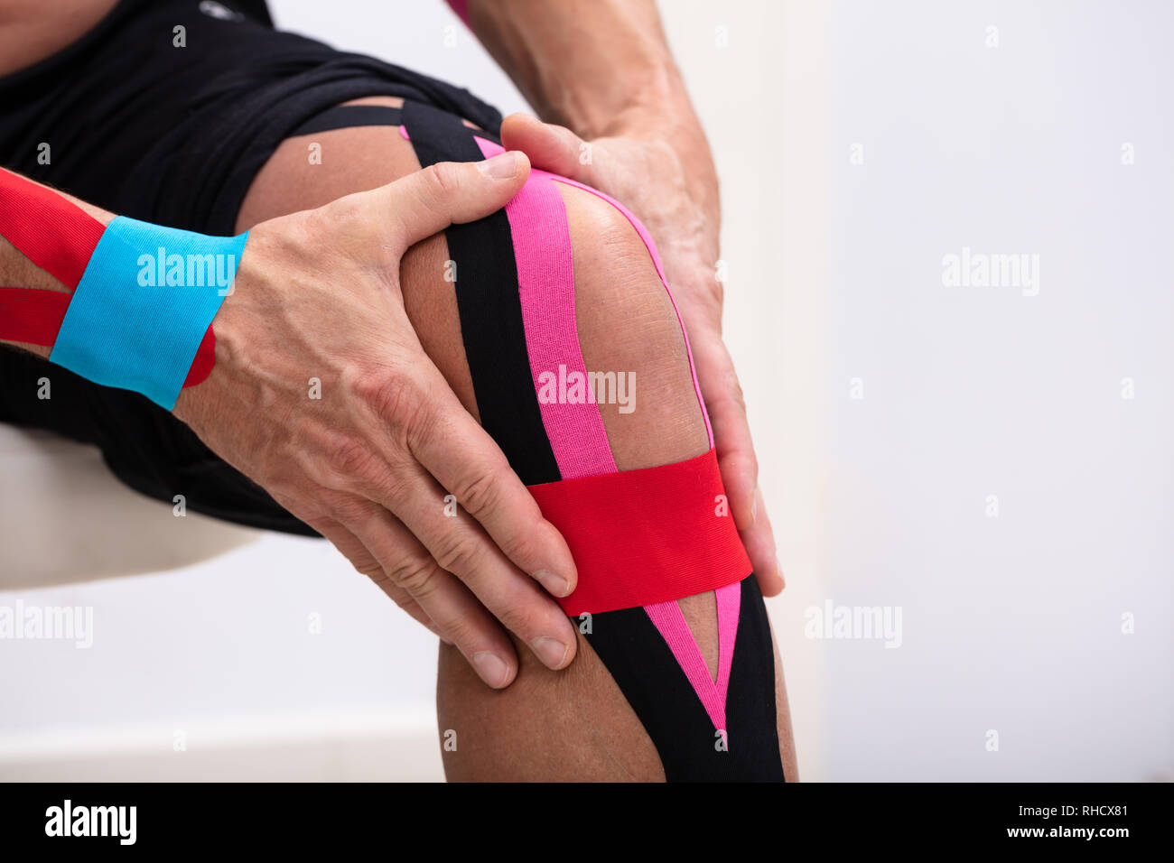Homme assis sur la table l'application de la kinésiologie tape sur son genou Banque D'Images