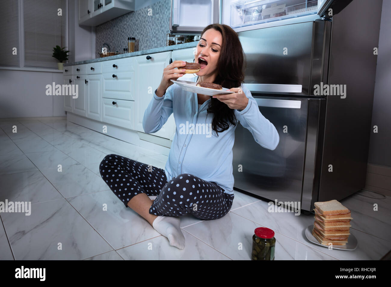 Young pregnant woman Eating Donut carrelage dans la cuisine Banque D'Images