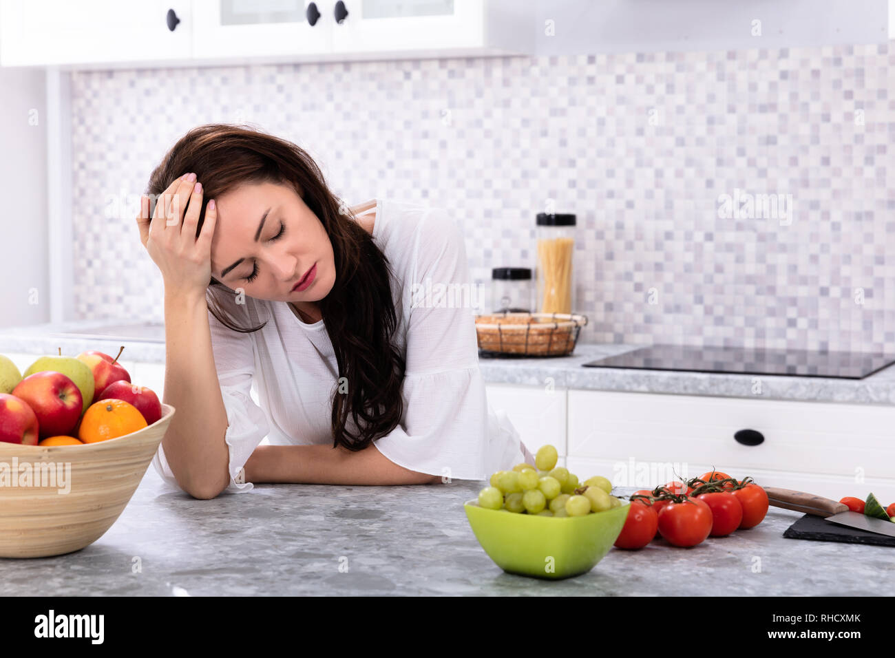 Fruits frais en face de contrarié Young Woman Leaning On Kitchen Counter Banque D'Images