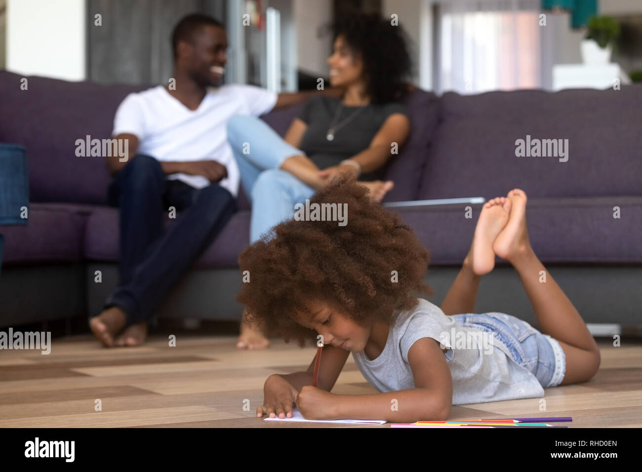 Fille de race mixte enfant dessin avec des crayons de détente avec les parents Banque D'Images