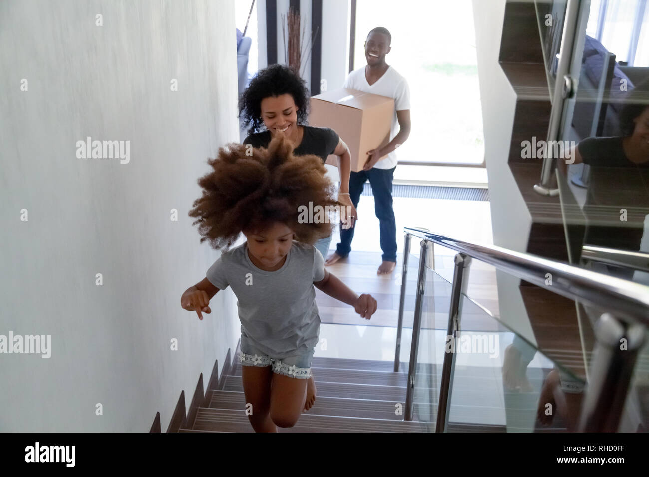 Heureux enfant noir tournant à l'étage déménagement avec les parents holding boxes Banque D'Images