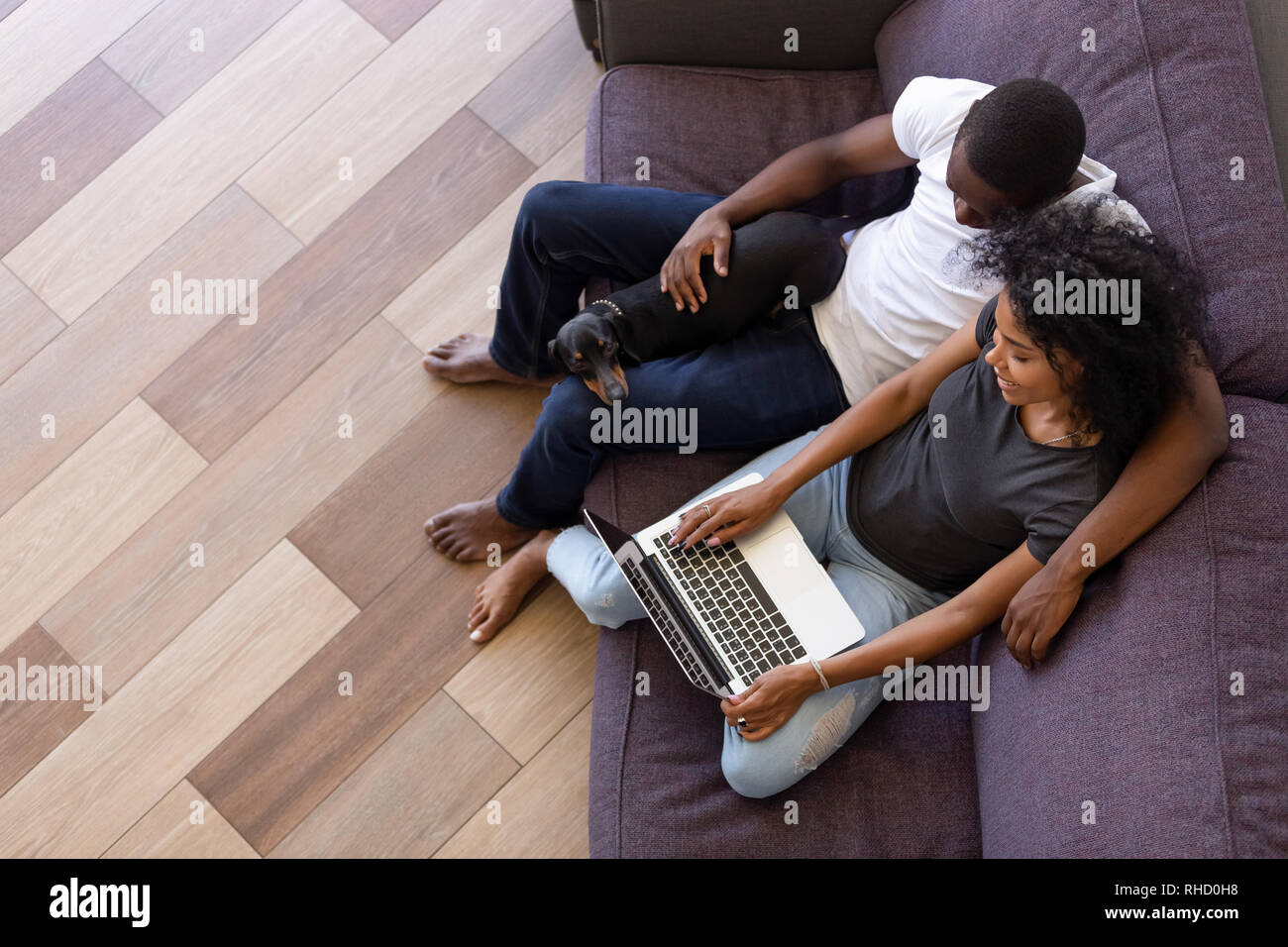 L'Afrique de l'heureux couple using computer sitting on sofa with pet Banque D'Images